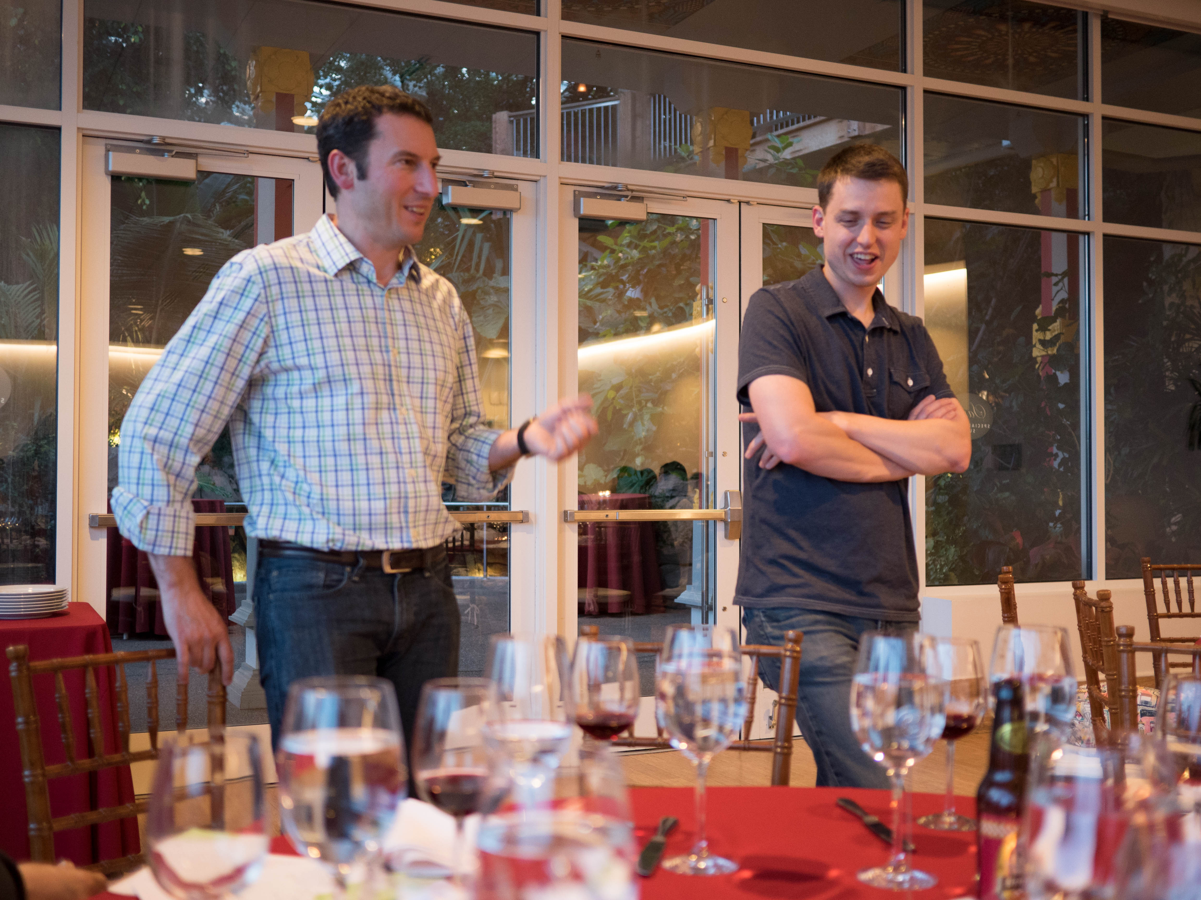 Two men chatting and laughing beside a dinner table set with wine glasses at the MLSS 2014 banquet